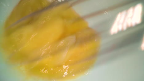 person scrambles chicken egg with metal whisk in white bowl