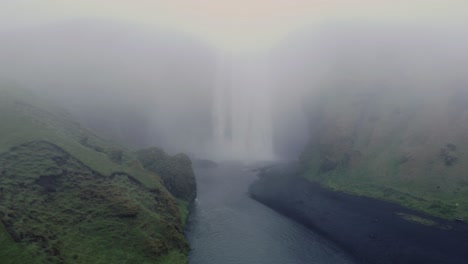 Moody-and-foggy-receding-drone-shot-of-Skogafoss-waterfall-in-Iceland