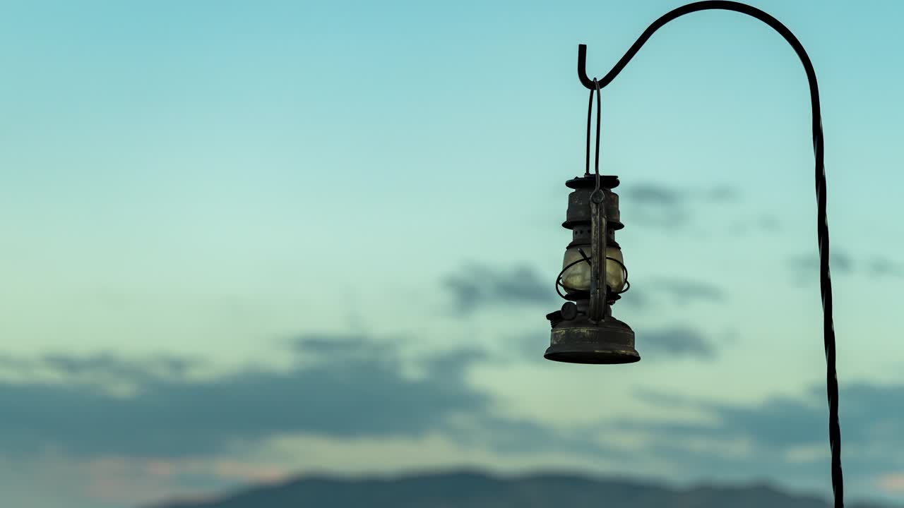 A vintage lantern hanging on a hook at sunset - time lapse zoom out to reveal the mountainous background
