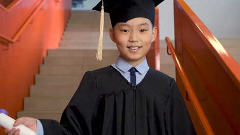 Retrato-De-Un-Feliz-Estudiante-De-Preescolar-Con-Toga-Y-Birrete-Sosteniendo-Un-Diploma-De-Graduación-Y-Mirando-La-Cámara-1