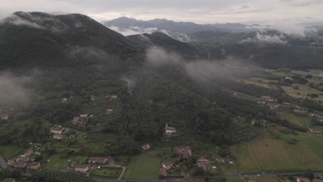 drone tiro de las nubes que se mueven más allá de la cámara en las colinas y montañas en italia en un día gris nublado con pueblos y casas en el suelo entre los campos verdes registro