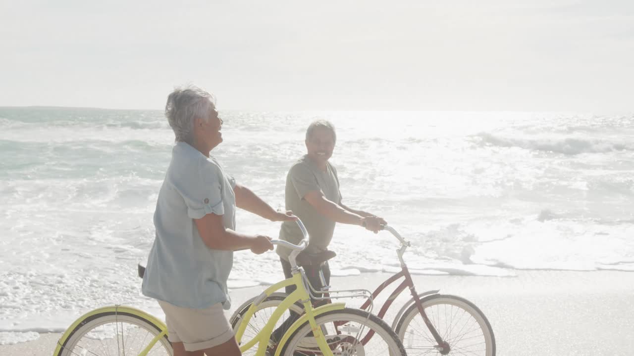해가 지는 해변에서 자전거를 타고  ⁇ 고 있는 행복한 히스패닉 시니어 커플의 측면 전망