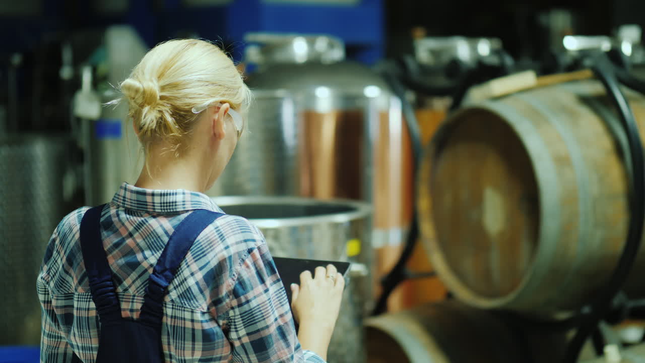 una mujer usa una tableta en un taller de bodega en el fondo hay barriles de madera