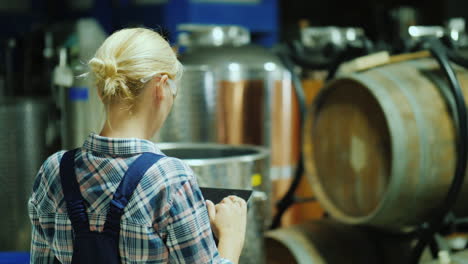 a woman uses a tablet in a winery workshop in the background are wooden barrels