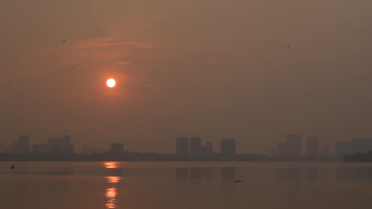 Sunset by the West lake in golden hour in Hanoi with orange sky and silhouette city far away