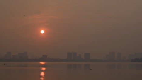 sunset by the west lake in golden hour in hanoi with orange sky and silhouette city far away