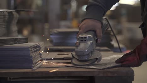 Worker-using-grinder-in-factory-on-metal-pieces