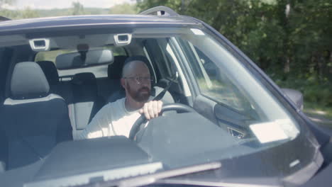 a bald man peacefully driving a subaru on a rural road