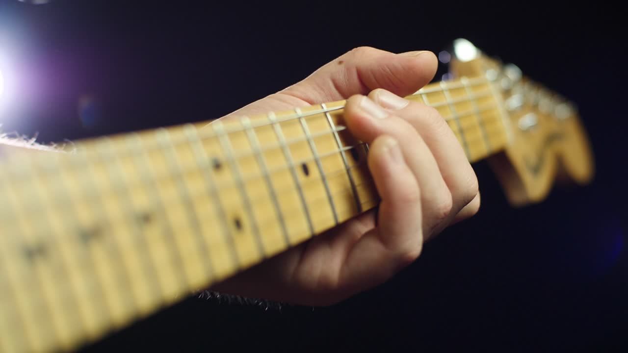 Slow motion close up of an electric guitars neck and strings and guitarists hands while playing notes. Smooth slow motion with gimbal forward movement, dark background. Shot in 4K at 120fps