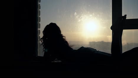 girl silhouette with curly hair lies on floor at sunset