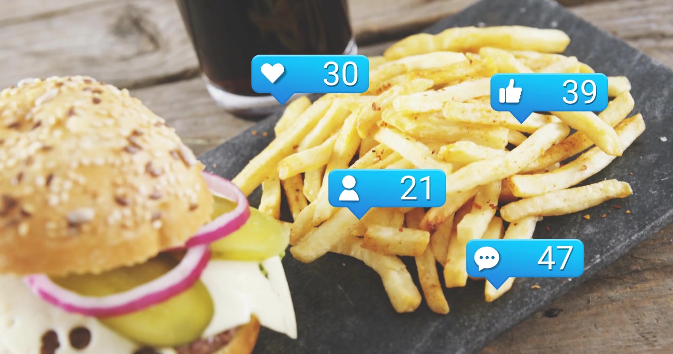 Vertical video: Fries, burger on slate, heart and like bubbles rising over food after post for ads