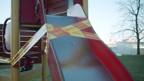 a closed down slide in an empty kids' playground wrapped in yellow and red "stop" caution tape due to quarantine