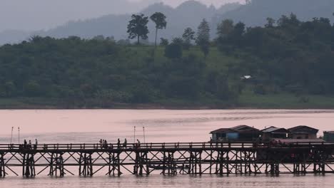 Mon-Bridge-and-a-longboat-followed-speeding-behind-the-structure-while-people-are-walking-on-the-bridge,-silhouetting-as-it-was-getting-dark,-in-slow-motion