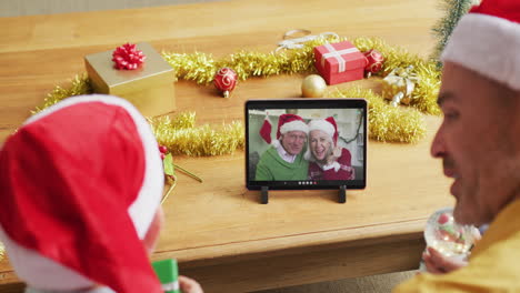 padre y hijo caucásicos con sombreros de santa usando una tableta para una videollamada de navidad con la pareja en la pantalla