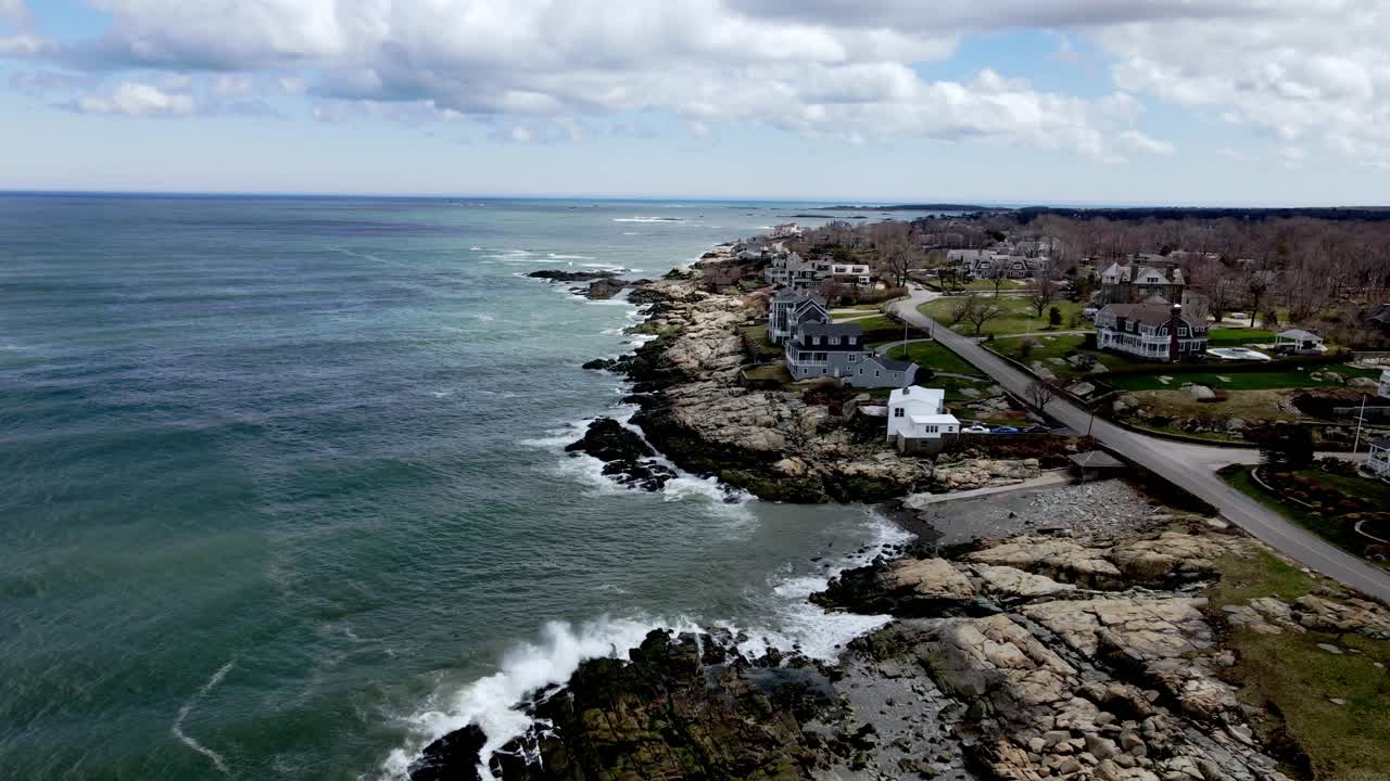 A static drone scene of houses looking out over waves, calmly crashing into a rocky coastline along the Jerusalem road on a cloudy day