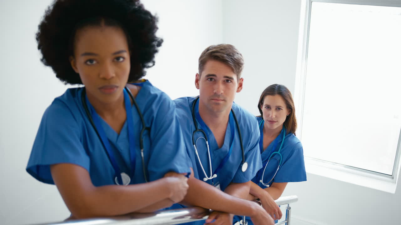 Portrait Of Serious Multi Cultural Medical Team Wearing Scrubs Standing On Stairs In Hospital