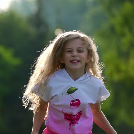 small cute girl with blond curly hair jumps happily in summer park. happy kid`s emotions outside. long hair of sweet girl