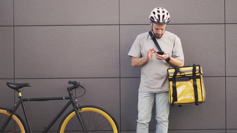 food delivery man with a thermal backpack consults an order on his smartphone 1