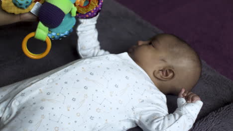 mother trying to entertain her 2 month old son laying on his back being by colourful plush toy