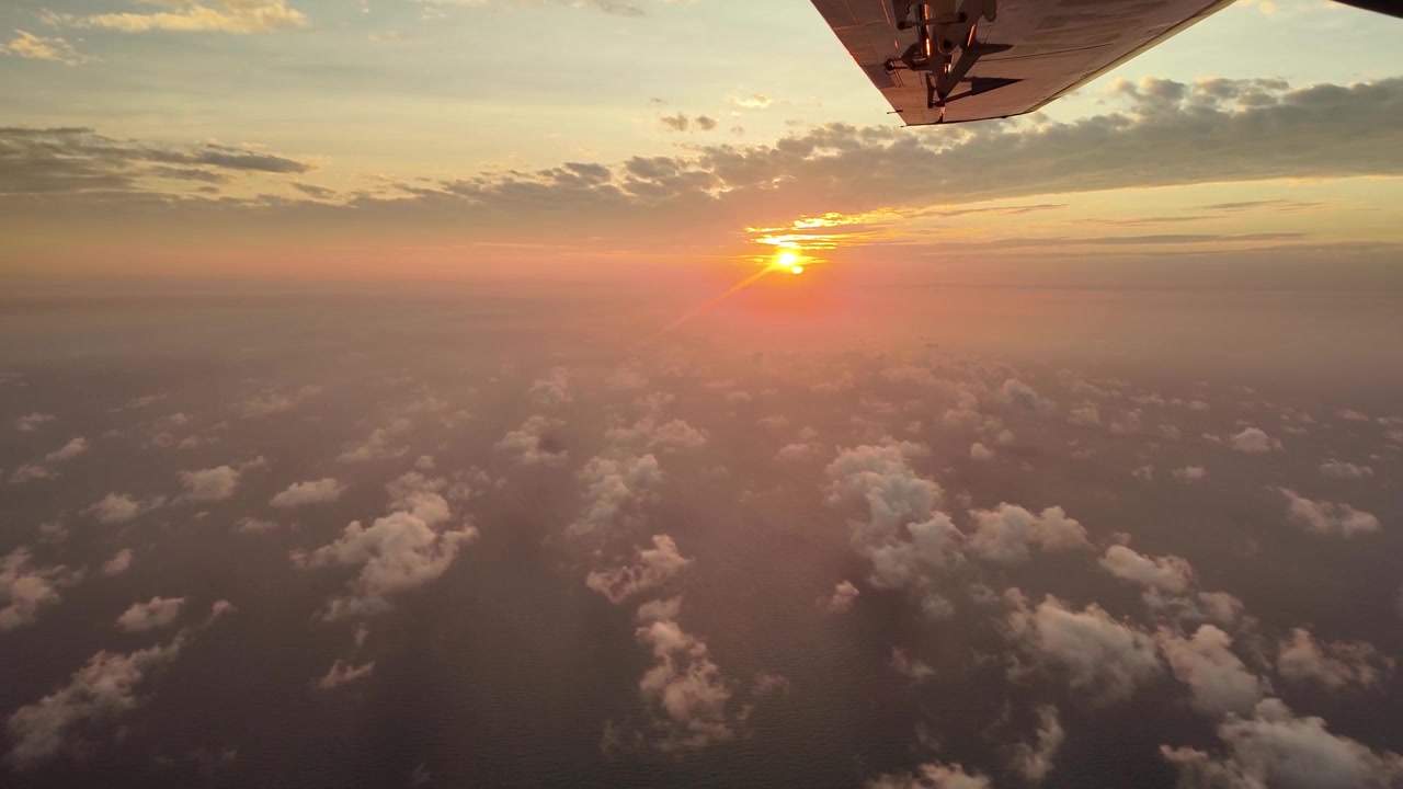 Tramonto sopra le nuvole visto dal finestrino di un aereo durante il volo.