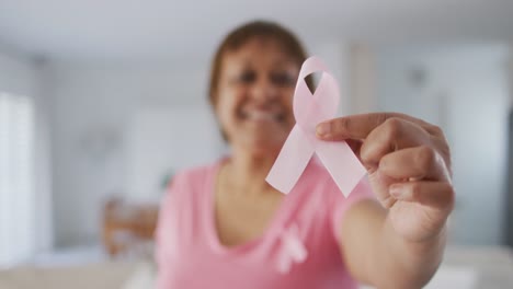 smiling african american senior woman wearing pink t shirt holding pink breast cancer ribbon