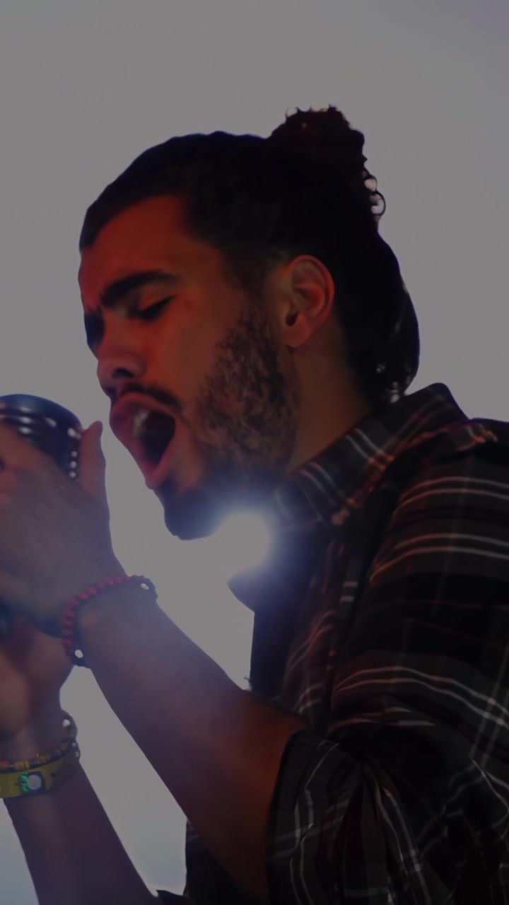 Vertical video: Male singer singing into mic, causing backlight flares and haze clearing for music