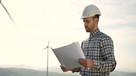 ingeniero caucásico con casco y viendo algunos planos en la estación eólica de energía renovable