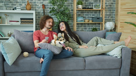 couple relaxing on sofa with dog and watching tv