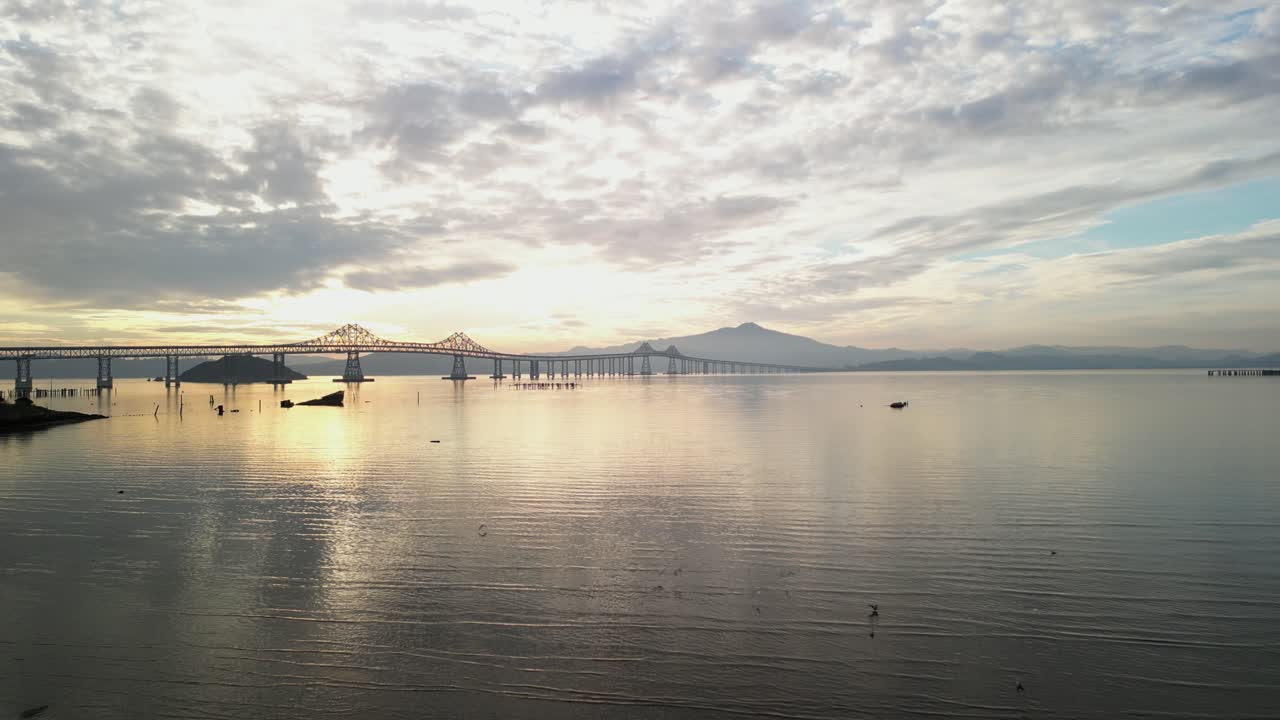 Backlit Richmond Bridge from Point Molate Beach Richmond California USA, aerial pullback as birds fly in low wetlands
