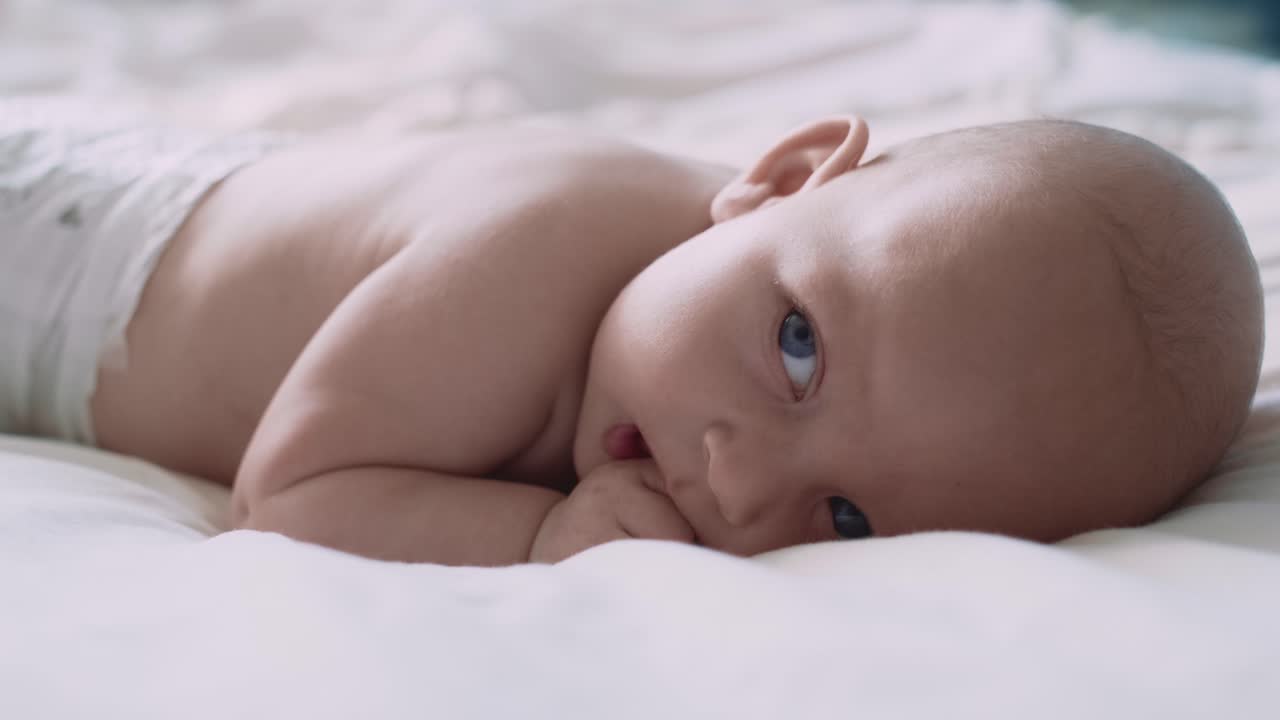 Nærbilde av nyfødt baby som ligger på magen i sengen og ser bort