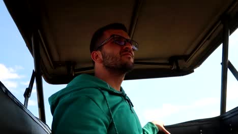 young man on a safari jeep backseat looking out for wild animals in africa