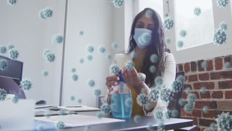 animation of covid 19 cells floating over mixed race woman wearing face mask disinfecting her hands