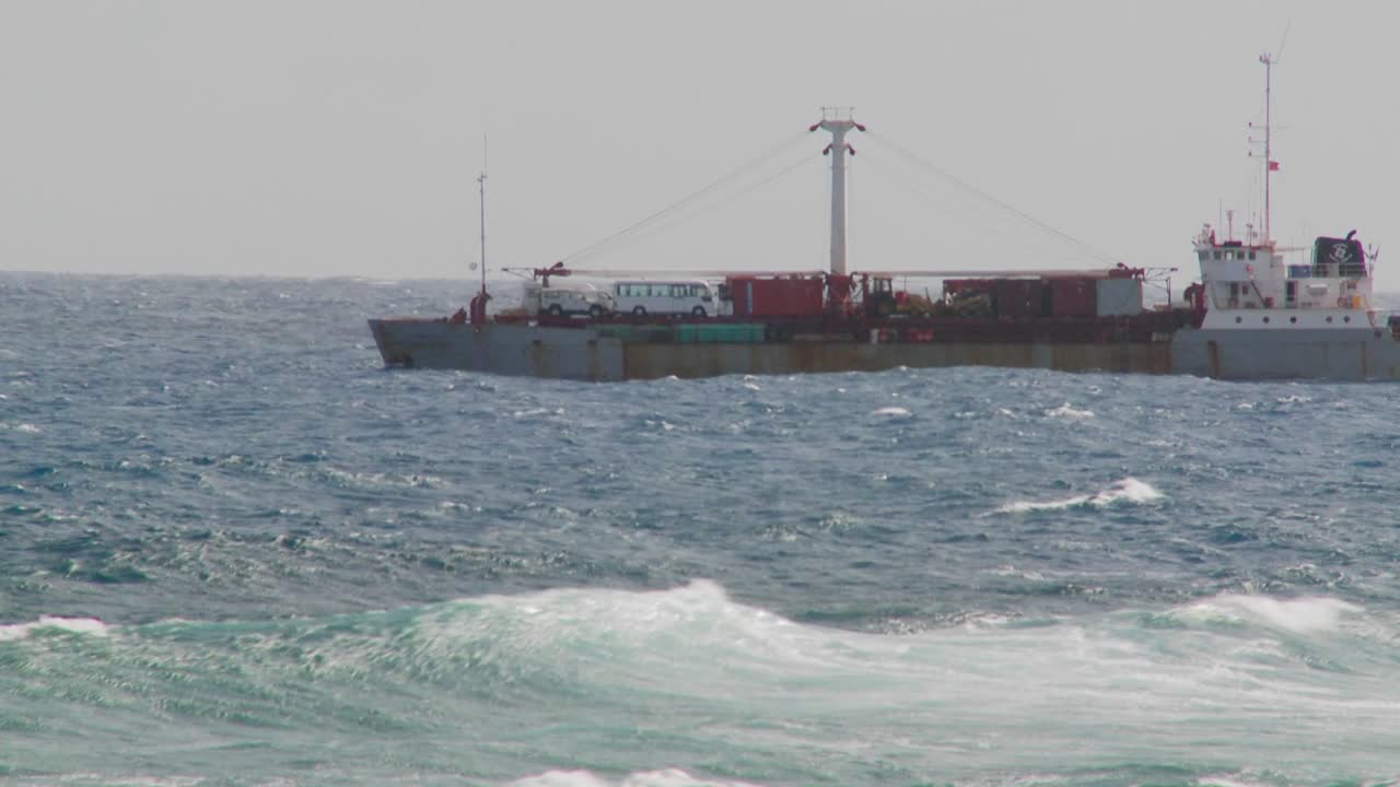 las olas ruedan hacia una costa rocosa con un carguero en el fondo 1
