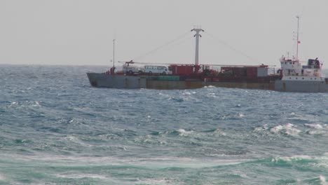 Waves-roll-into-a-rocky-shore-with-a-freighter-ship-in-the-background-1