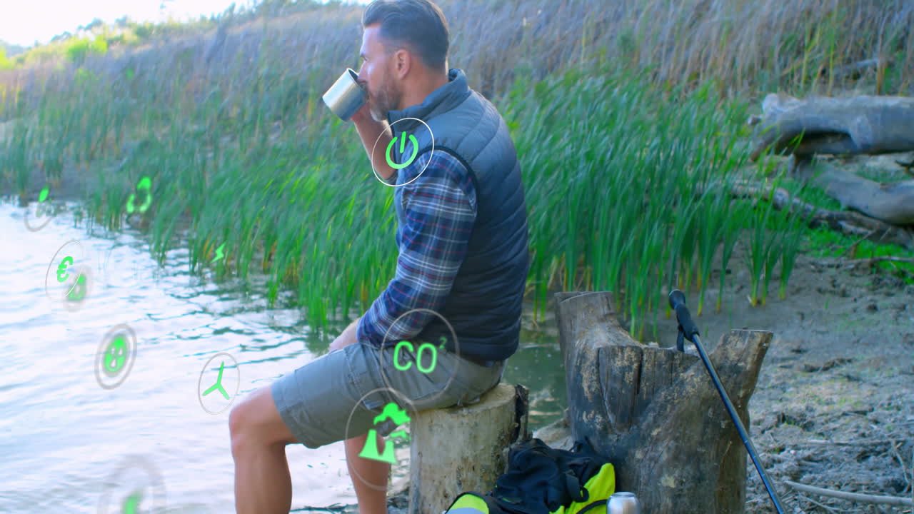 Man sitting on stump sipping from mug beside lake, showing floating green AR renewable energy icons