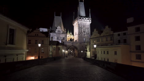 Una-Vista-De-Una-Torre-De-Puerta-Gótica-En-Un-Extremo-Del-Puente-De-Carlos-En-El-Centro-Histórico-De-La-Ciudad-De-Praga-Por-La-Noche-Durante-Un-Cierre-Covid-19-Sin-Gente-En-Ninguna-Parte,-Arquitectura-Pintoresca,-Tiro-Inclinado-De-4k