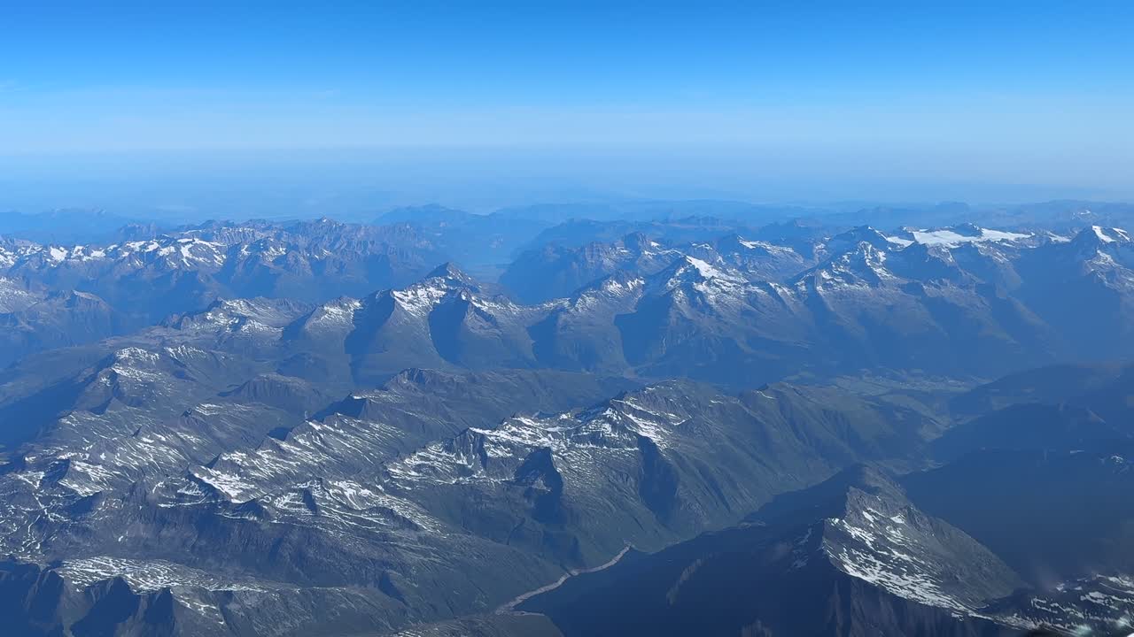 An elevated aerial view of the Swiss Alps mountains taken from an airplane cabin flying at 11000m high in a hazy summer morning.