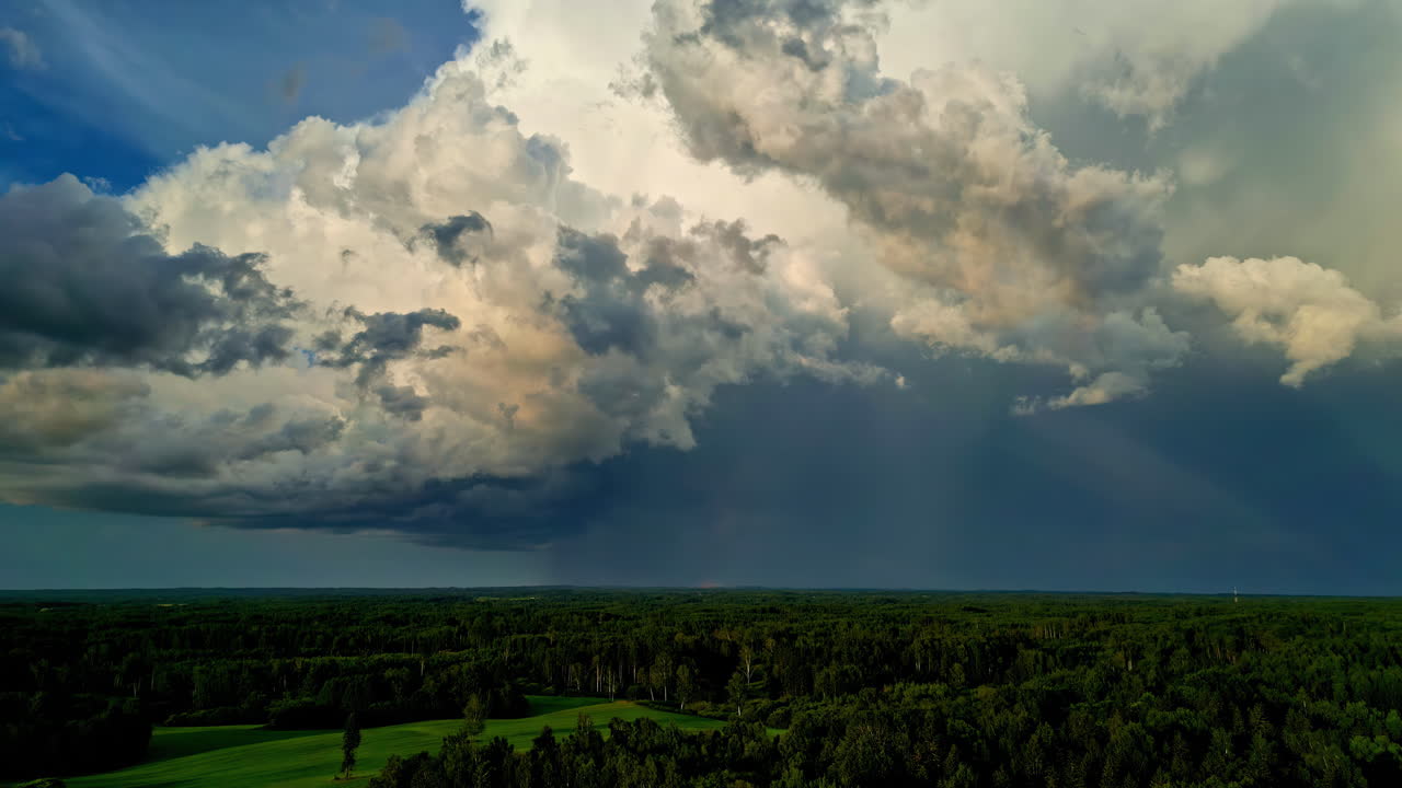 Cumulonimbus clouds forming while raining over green field. Time lapse