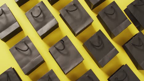 Reihen-Schwarzer-Geschenktüten-Mit-Schwarzen-Kordelgriffen-Auf-Gelbem-Hintergrund