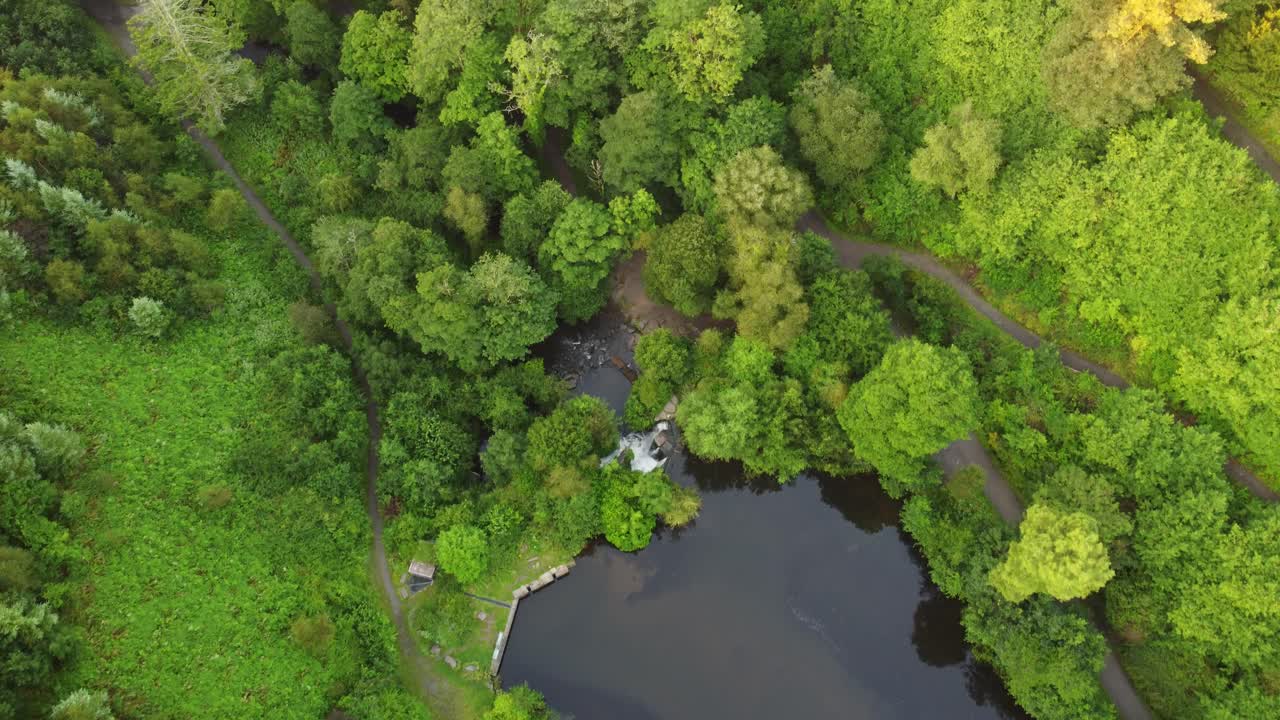 Vue aérienne au-dessus d'un lac menant à une cascade et une rivière, avec une forêt dense dans une vallée.