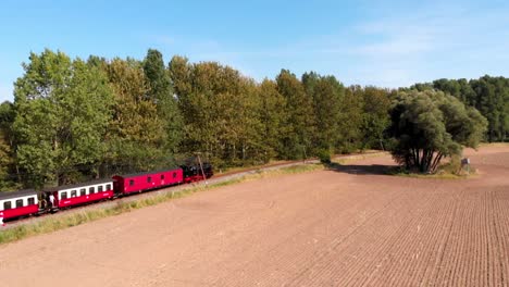 aerial: steam narrow gauge railway in the countryside passing by sown fields and some trees