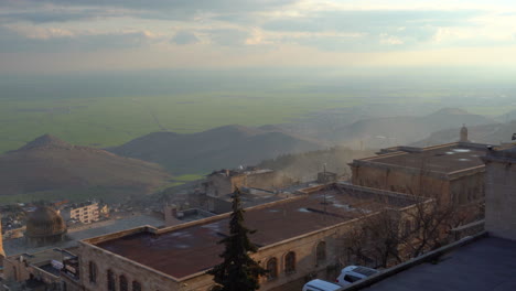 Mardin-Ulu-Camii's-minaret-from-Zinciriye-Medrese-on-a-sunny-day-over-looking-Mezopotamia,-wide-open-green-fields-from-the-historical-buildings