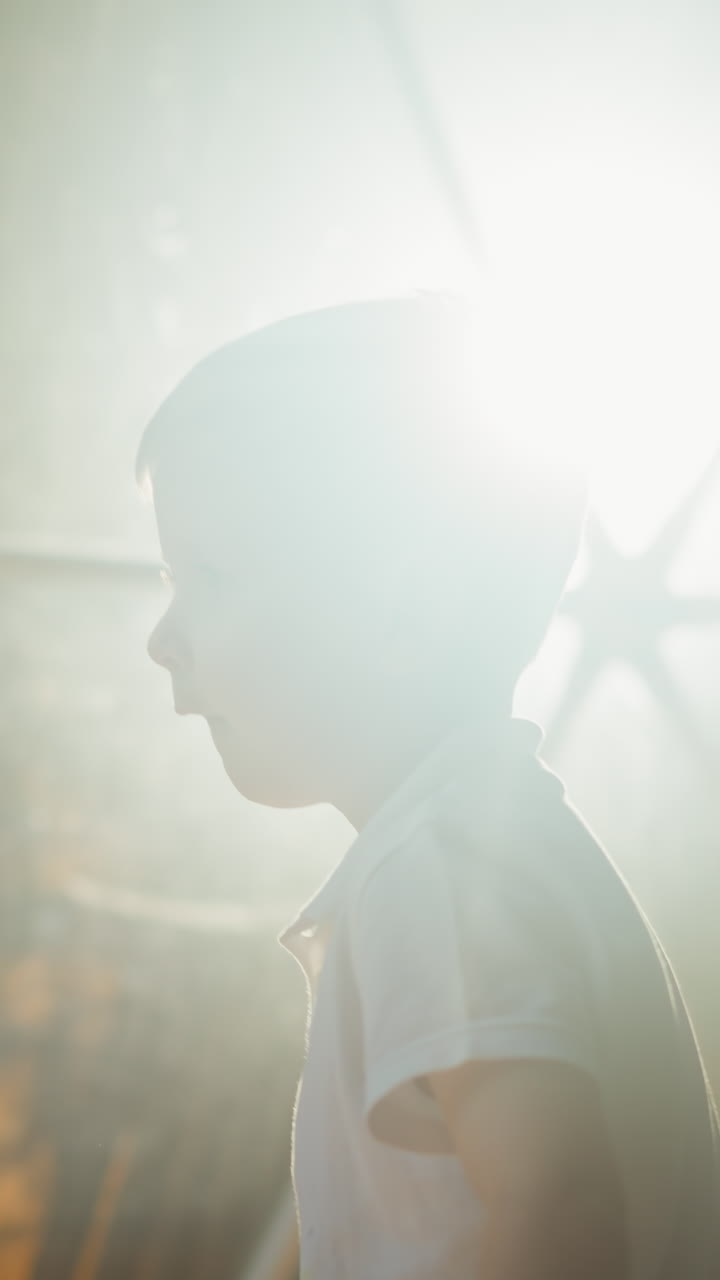 작은 아이는 텐트 창문 뒤에 랜턴의 빛에 대항하여 서 있습니다. 피곤한 귀여운 유치원 아이는 밤에 휴양지에서 휴식을 취합니다.