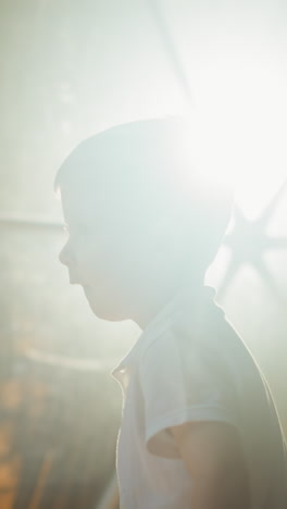 small kid stands against light of lantern behind tent window. tired cute preschooler goes to rest in evening at resort on glamping area slow motion backside view closeup