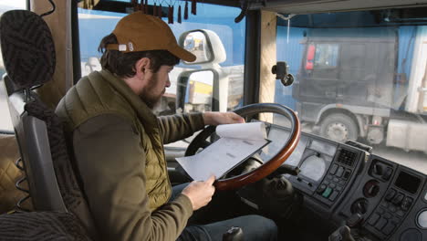 side view of worker sitting in a truck in a logistics park while reading documents