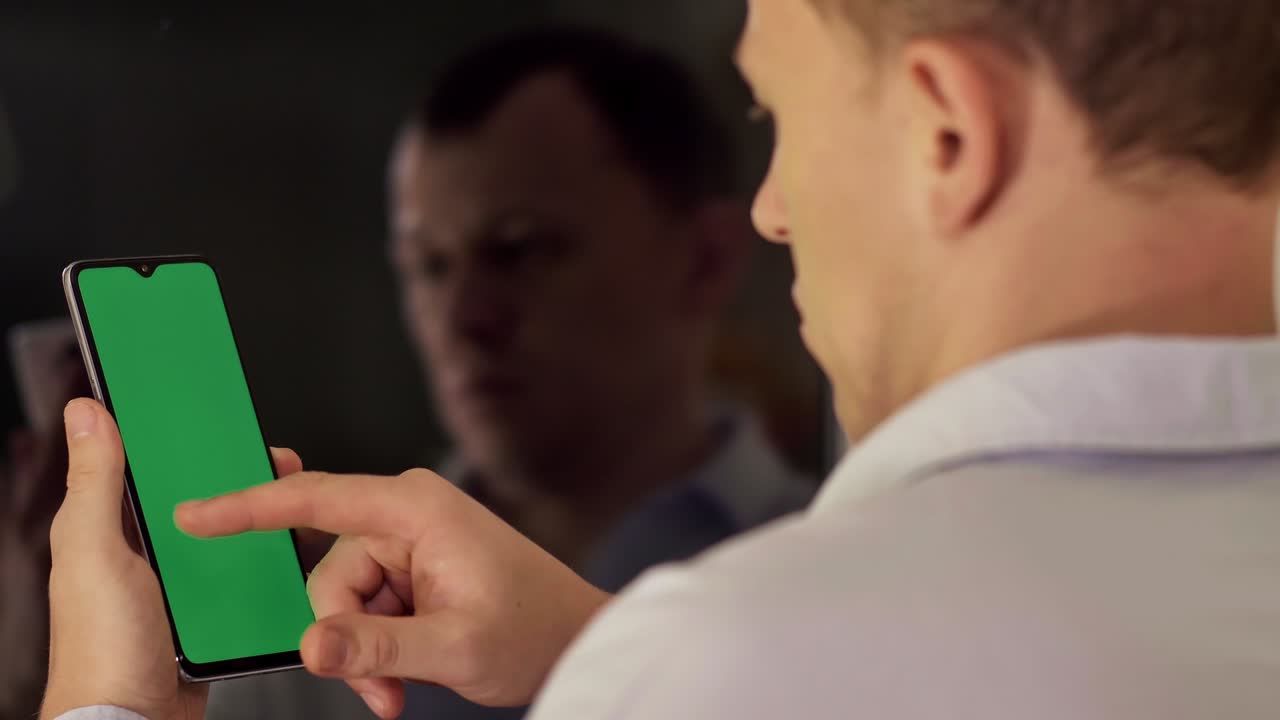 Young man with a phone moves his finger across the screen, chroma key, back view, reflection in the mirror