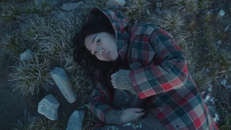 portrait of young woman lying on dry grass and holding lantern at dusk