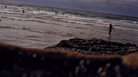 sunny summer day. people are swimming in waves not far from a shore. boy, dressed in wet suite is walking in sea water along a rocky beach location in cornwall, uk. footage in hd