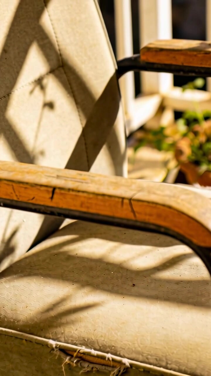 Vertical video: Shifting camera revealing worn armchair on porch, frayed seam and plant shadows