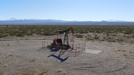 oil pumpjack in the arid plains of malargüe, argentina, with the andes mountains rising in the background under a clear blue sky.